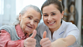 Seniorin und Altenpflegerin lächelnd mit Daumen nach oben